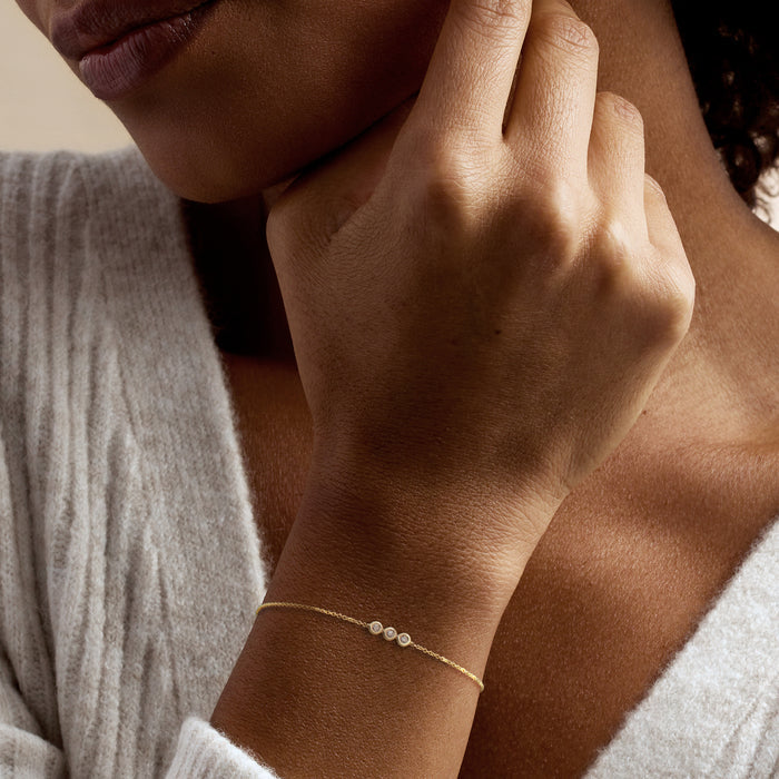 Yellow gold bracelet with small round diamond bezels on wrist and fine chain