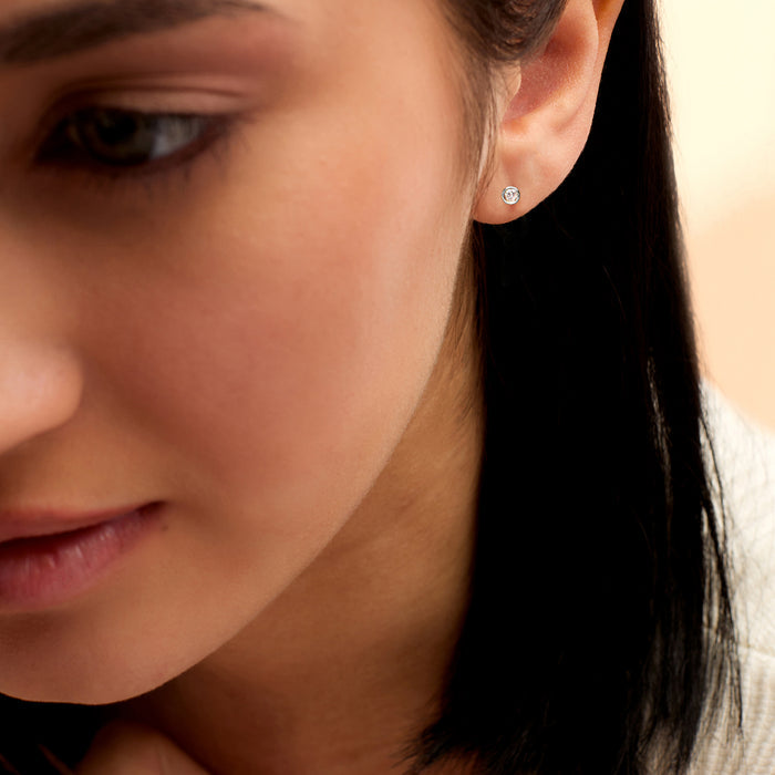 Sterling silver diamond stud earrings on ear, round bezel-set stones