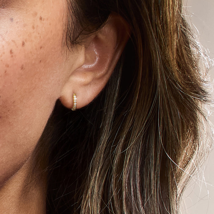 Gold huggie hoop earrings with diamond row worn on ear