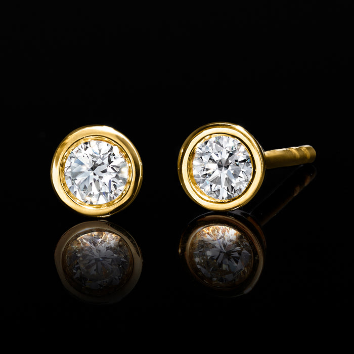 Lab-grown diamond stud earrings with round bezel-set stones, gold bezel and posts.