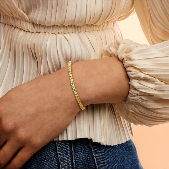 Gold bead stretch bracelet with small green gem accents on wrist