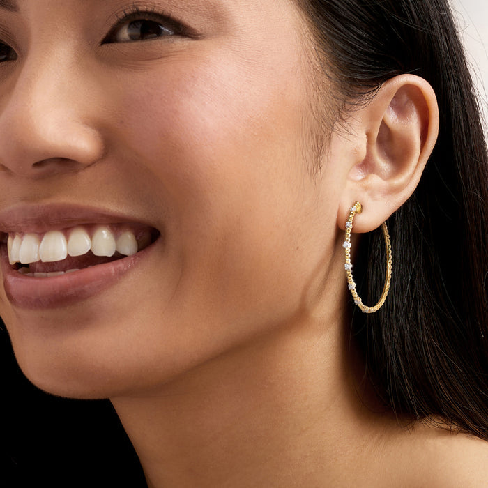 Diamond station beaded hoop earrings on ear, gold hoops with small sparkle stones