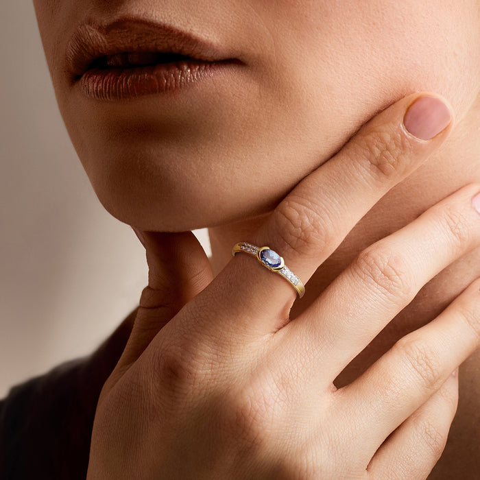 Gold oval blue gemstone ring with white zircon band worn on finger