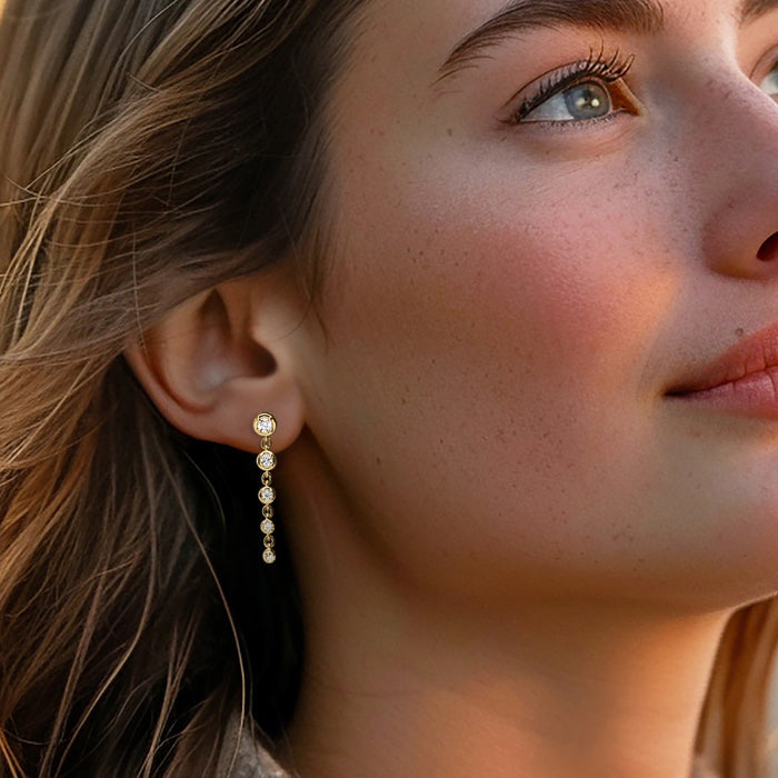 Gold diamond drop earrings on model, featuring small round bezel-set stones